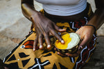 Ghanian lady in tradtitional outfit holding a wodden bowl filled with white and yellow borututu shea butter