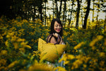 Woman holding a yellow woven bag in a forest with yellow flowers