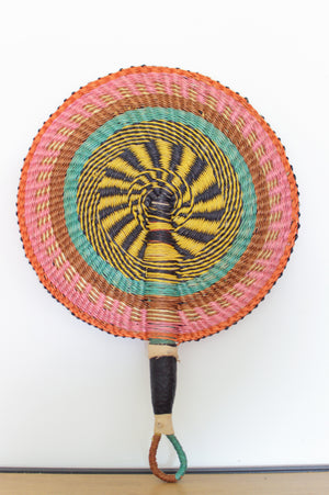 
                  
                    pastel colored round bolga basket with leather handle on a white wall
                  
                