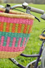 pastel colored bolga bike basket with leather straps attached to a bike handle