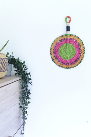 
                  
                    pastel colored round bolga fan hanged on a white wall
                  
                