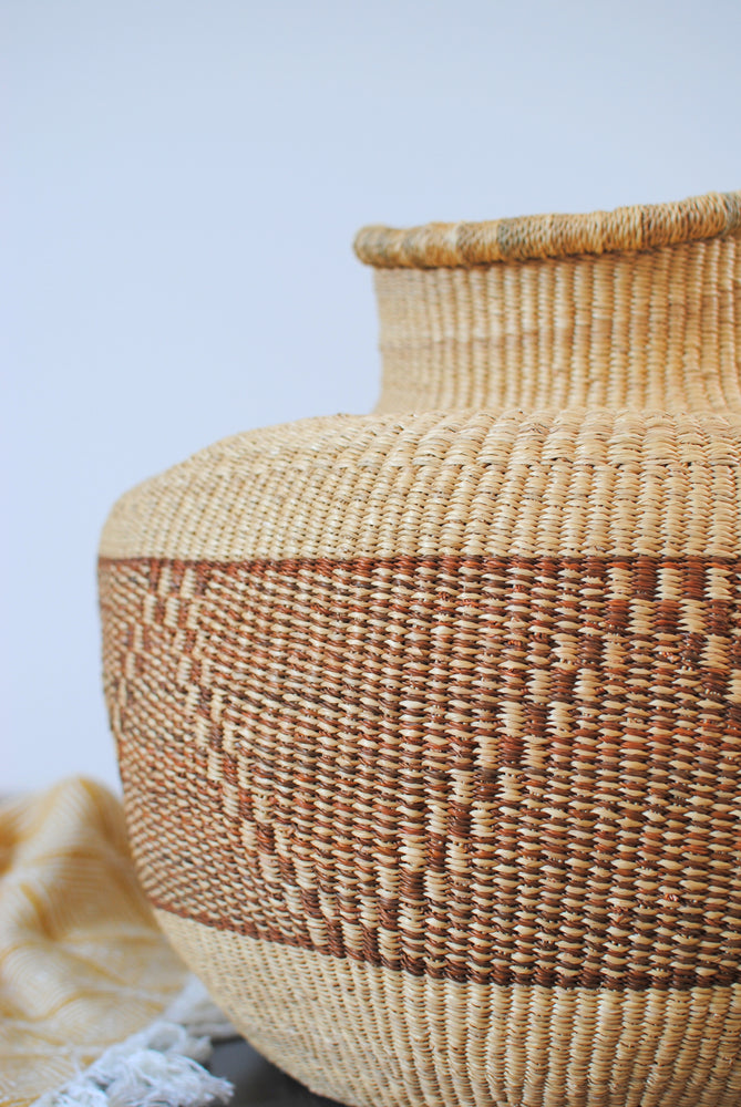 a close up of a large vase straw basket in natural colors on a table